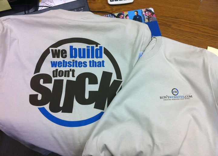 Two light brown tee shirts with the words "we build websites that don't suck" in blue and brown